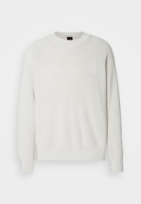 Bílá svetr s ribovanou pleteninou a kulatým výstřihem, dlouhými rukávy. Malá nášivka s logem na hrudi. Měkká textura, volný střih.