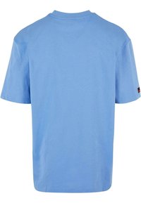 Tricou scurt cu mânecă scurtă de culoare albastru deschis, cu gât clasic și tiv drept. Prezintă un mic etichete negre pe mâneca stângă.