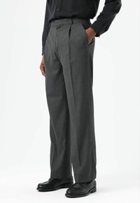 Grijze, op maat gemaakte broek met plooien, gemaakt van textuurbroekstof. Voorzien van zijzakken en een relaxte pasvorm, gecombineerd met zwarte loafers.