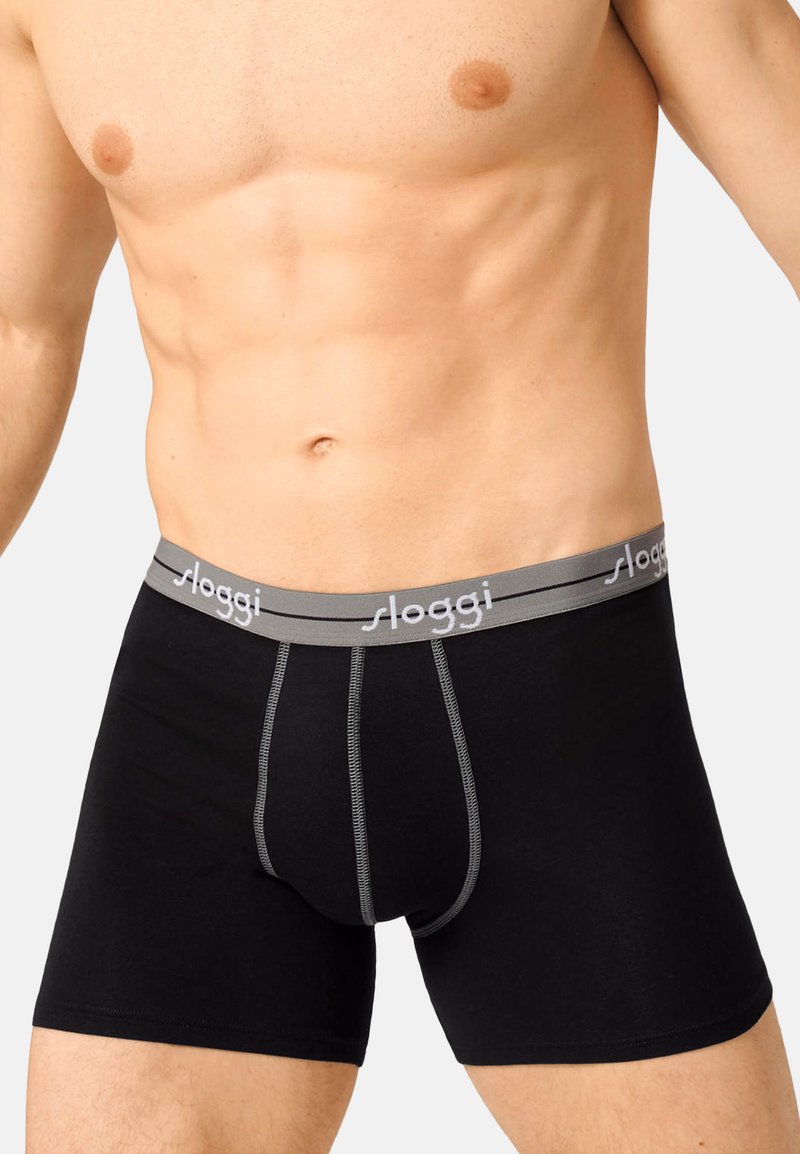 Schwarze Boxershorts mit einem grauen Bund, der mit dem "sloggi"-Logo versehen ist. Der Stoff wirkt glatt mit kontrastierenden Nähten. Sitzt eng an.