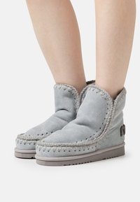 Botines de ante gris con un puño doblado, costuras decorativas a lo largo de las costuras y una suela de goma texturizada.