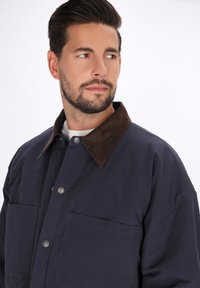 Marinejacke mit einem braunen Cordkragen, Frontdruckknöpfen, zwei Brusttaschen und lockerem Schnitt. Glatte Stofftextur.