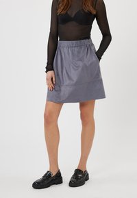 Gonna grigia in suede con vita elasticizzata, taglio dritto e dettagli delle cuciture, abbinata a mocassini neri lucidi.