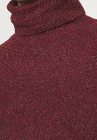 Burgundy turtleneck sweater with a textured, knit design. Fabric has a soft, warm appearance with subtle speckles in darker tones.