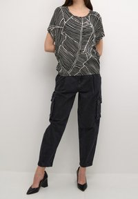 Schwarz-weiß gemustertes Kurzarm-Oberteil mit lockerem Sitz, kombiniert mit dunklen Cargohosen und schwarzen Schuhen mit Absatz. Glatte Textur, lässiges Design.