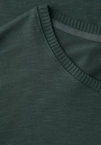 Tessuto a maglia verde scuro con collo a costine. Texture liscia con un sottile motivo melange, che enfatizza morbidezza e flessibilità.