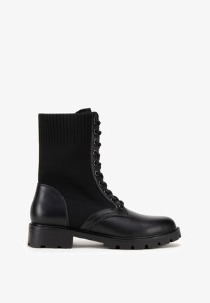 Zwarte enkellaarsjes van een combinatie van leer en ribbeltricot, met een ronde neus, vetersluiting aan de voorkant en een lage blokhak.