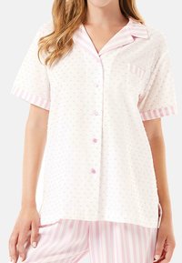 Camiseta de pijama de manga corta en tejido suave y ligero; blanca con lunares rosas y detalles a rayas, con un cierre de botones en la parte delantera y un bolsillo.