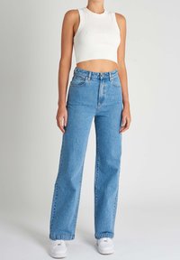 Valkoinen ribattu cropped toppi, joka on yhdistetty korkeavyötäröisiin vaaleansinihin farkkuihin. Farkuissa on klassinen suora lahje ja viisi taskua.