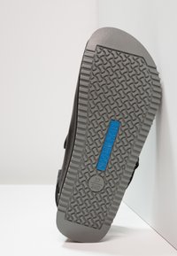 Sandal nera con suola in gomma testurizzata, caratterizzata da un'etichetta con logo blu e un motivo a contrasto grigio sulla suola per una maggiore aderenza.