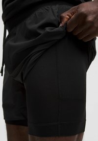 Pantaloni sportivi neri con un tessuto testurizzato e traspirante. Presentano una vita elasticizzata e dettagli di cuciture visibili.