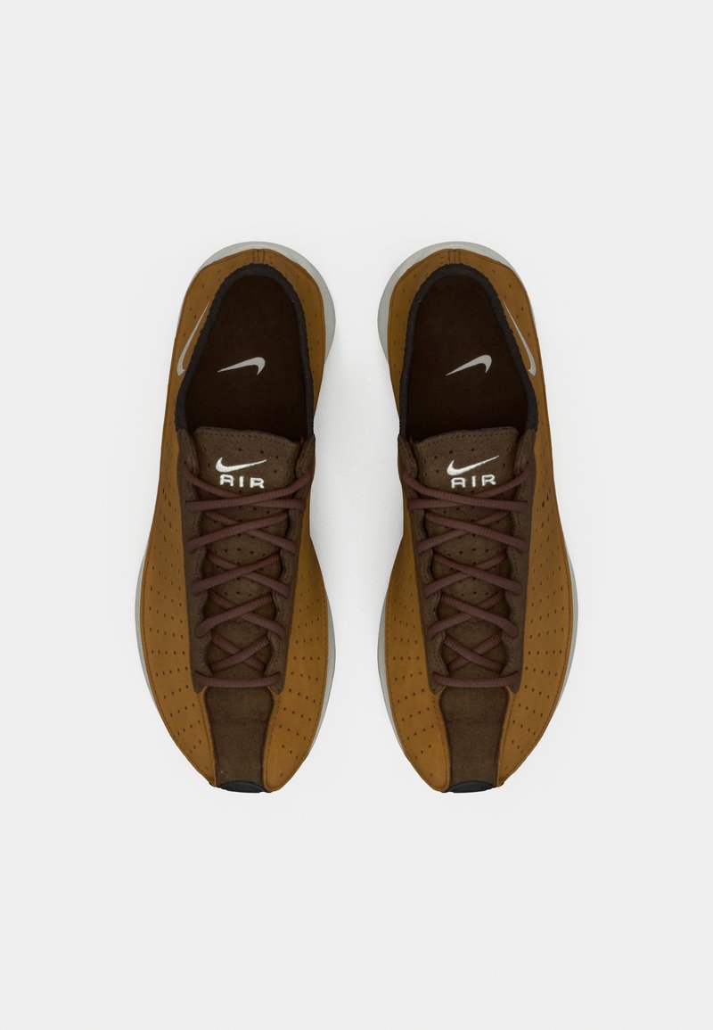 Baskets perforées marron avec des accents et des lacets marron foncé. Présente un logo Nike blanc et une semelle texturée. Design à bout rond.