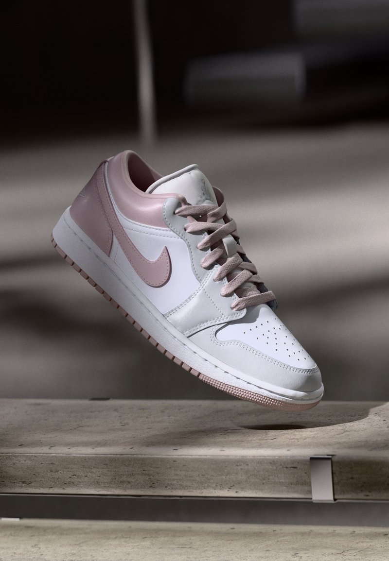 Baskets Nike blanches et rose clair flottant au-dessus d'une surface en béton avec des ombres en arrière-plan.