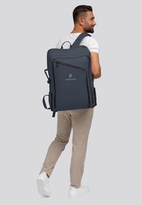 Grand sac à dos bleu marine avec plusieurs compartiments, fermetures éclair noires et un logo. Équipé de bretelles rembourrées et de poches latérales.