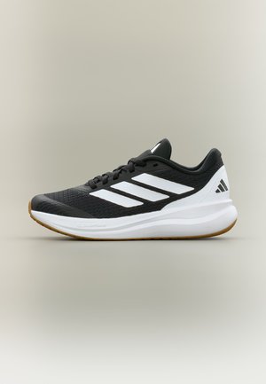 Scarpa da corsa Adidas bianca e nera con strisce bianche, suola ammortizzata e suola marrone su sfondo beige.