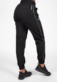 Zwarte joggingbroek van zacht materiaal, met een hoge taille, tapered ontwerp, witte zijkanten en elastische cuffs bij de enkels.