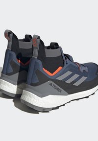 Blaue und graue Wanderschuhe mit gestrickter schwarzer Knöchelstütze, orangenen Akzenten, reflektierenden Details, strukturierten Sohlen und Terrex-Branding.