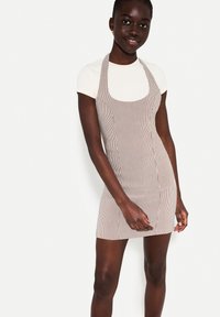 Gestreepte schortstijl jurk in lichtbruin en wit, met een vierkante halslijn, een aangesloten vorm en twee zijzakken. Glad textuur van de stof.