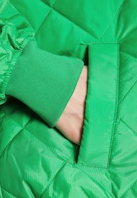 Hand in de zijzak van een felgroene gewatteerde jas met elastische manchetten.