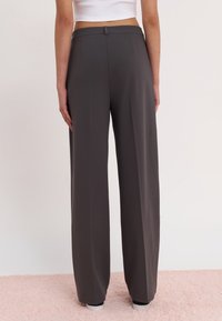 Pantalon gris à jambes larges en tissu lisse et léger. Caractérisé par un design épuré, une taille plate et sans poches visibles.