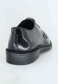 Scarpa in pelle nera con finitura lucida, punta rotonda, tacco basso e design con lacci. Presenta una cucitura decorativa vicino alla parte posteriore.