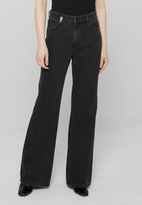 Jean noir à jambes larges en denim, doté d'un design classique à cinq poches, de passants pour ceinture et d'une fermeture à bouton à la taille.