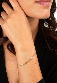 Guldfärgad armband med delikata kedjelänkar med växlande solida och ihåliga ovala former, buren på ett handled med slät hud.