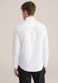 Balta krekls ar garām piedurknēm, pogām ap kaklu, noapaļotu apakšmalu un pogātām piedurknēm. Izgatavots no gludas auduma ar klasisku piegriezumu.