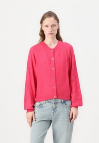 Rosa ribbad kofta med rund halsringning, silverfärgade hjärtformade knappar och långa ärmar, i kombination med ljusblå jeans.