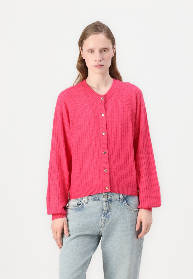 Rosa ribbad kofta med rund halsringning, silverfärgade hjärtformade knappar och långa ärmar, i kombination med ljusblå jeans.