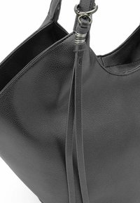 Zwarte leren tote bag met een gestructureerd oppervlak, ruime interieur en decoratieve metalen hardware op de strap. Minimalistisch ontwerp.