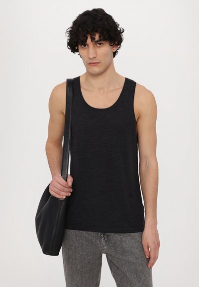 Débardeur noir sans manches en tissu doux, porté avec un jean gris. Le modèle tient un sac en cuir noir à la texture lisse.
