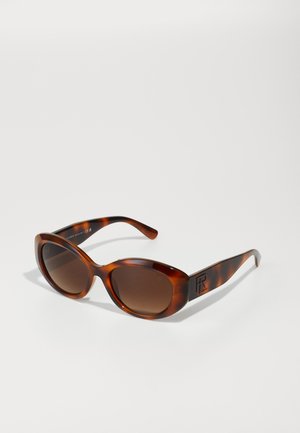 Brown tortoiseshell sunglasses with curved lenses, thick frames, and a logo detail on the temple. Gradient lenses provide UV protection.