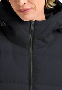 Zwarte gewatteerde jas met een hoge kraag, ritssluiting en duurzaam materiaal; beschikt over een subtiele gestikte textuur en verstelbare hardwareaccenten.