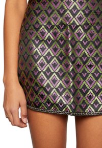 Metalen minirok met een geometrisch patroon van paarse, groene en zwarte driehoeken, met een zwarte draadzoom.