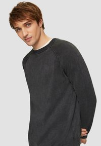 Kohlegrauer Sweatshirt, Rundhalsausschnitt, weicher Stoff, gerippte Bündchen und Saum. Detailnaht an den Schultern. Das Model steht leicht seitlich gedreht.