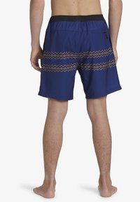 Shorts de bain bleus avec un motif en zigzag texturé rouge et gris, dotés d'une taille élastique et d'une poche zippée sur le côté.