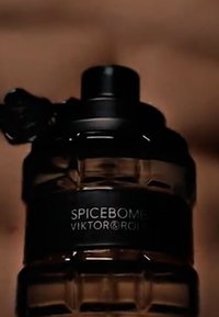 Flacon de parfum noir en forme circulaire avec un verre texturé, présentant une section inférieure transparente, et une étiquette noire mate portant l'inscription "SPICEBOMB VIKTOR&ROLF."