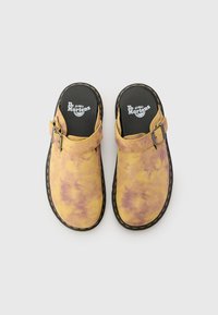 Yellow and purple tie-dye clogs, featuring a wide strap with a buckle, textured suede material, and black rubber soles with yellow stitching.