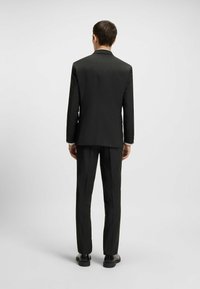 Black pinstriped suit featuring a single-breasted jacket and straight-leg trousers, complemented by sleek black shoes. Smooth texture.
