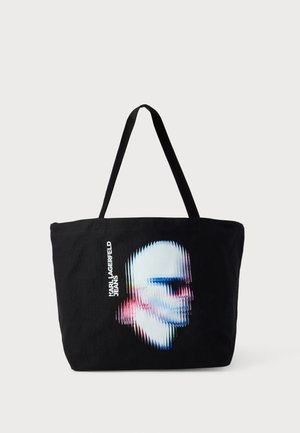 Crna torba za nošenje napravljena od tkanine, s iskrivljenim grafikonom lica u bijeloj boji s plavim i ružičastim naglascima. Uključuje tekst "KARL LAGERFELD JEANS".