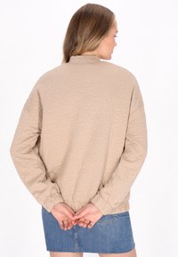 Beige textúrájú dzseki virágmintával, magas gallérral és gumírozott mandzsettával, középmagas szoknyával párosítva.