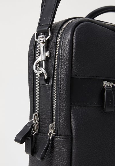 Sac en cuir noir avec un extérieur texturé, des fermetures éclair en argent et des tirettes en cuir noir. Comprend une bandoulière amovible et une forme structurée.