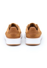 Un paio di sneaker in pelle beige con suole a piattaforma bianche, viste da dietro su uno sfondo bianco.