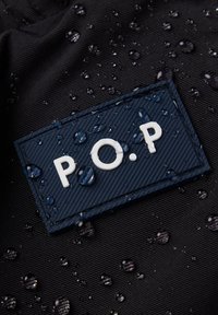 Laikka tummasta kankaisesta materiaalista, jossa on valkoiset kirjaimet "P.O.P." vedenpisaroiden ympäröimänä rakenteellisella pinnalla.