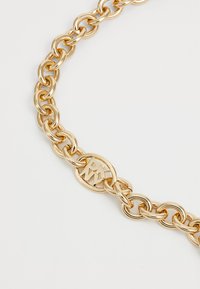 Collier en métal doré avec une grande chaîne à maillons entrelacés et un fermoir ovale gravé du logo. Surface lisse et brillante avec une finition polie.