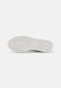 Suela blanca de zapato con un patrón de panal texturizado, que presenta líneas onduladas y un logotipo en relieve. Borde liso y material flexible.