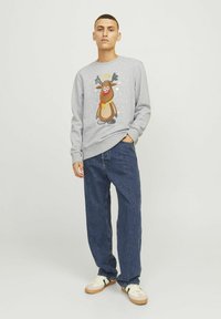 Grijze sweatshirt met een cartoon rendier met takken en een rode neus, gecombineerd met donkerblauwe jeans en witte sneakers. Eenvoudig ontwerp.