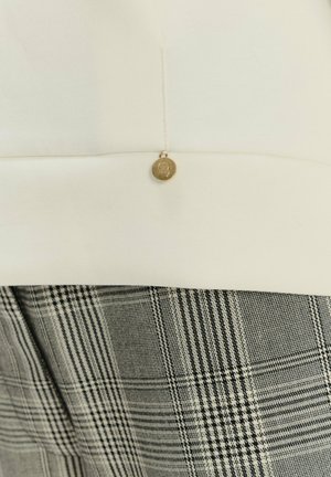 Top blanco con escote redondeado, adornado con un botón dorado; combinado con pantalones de cuadros grises que presentan un patrón texturizado.