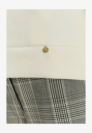 Top blanco con escote redondeado, adornado con un botón dorado; combinado con pantalones de cuadros grises que presentan un patrón texturizado.